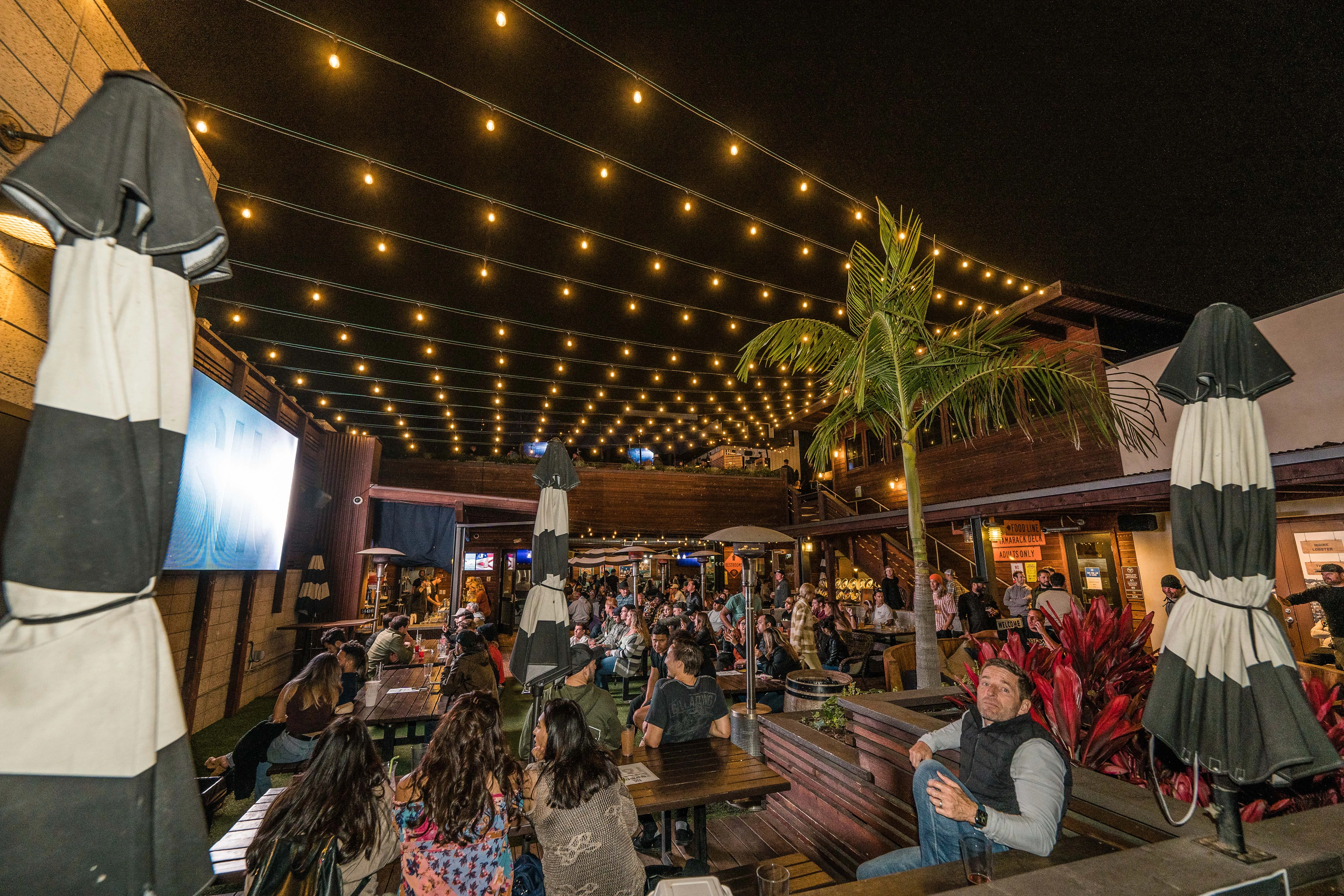 Fans watching a football game on the outdoor LED screen at Park 101 Carlsbad with string lights overhead